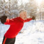 Outdoor winter sports. Happy senior man training with fitness straps at sunny snowy park, free space